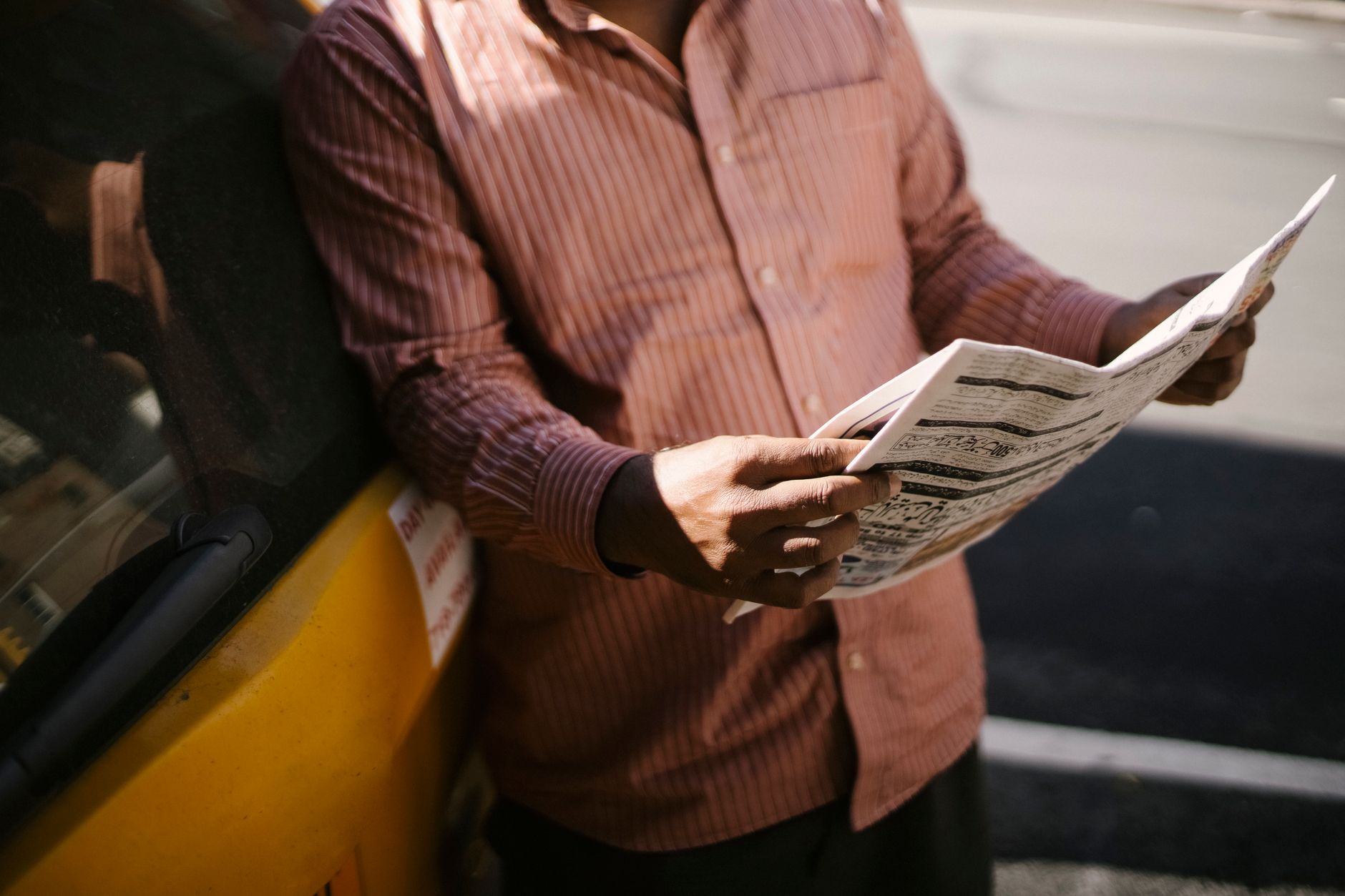 Crop anonymous ethnic cab driver in ornamental shirt standing with newspaper near transport in sunlight — Expert Strategies f