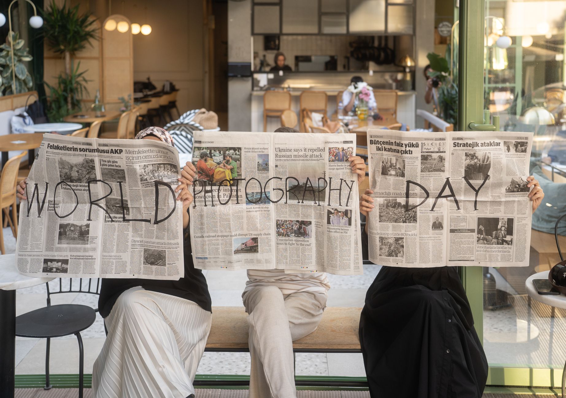 Three people holding newspapers promoting World Photography Day in a cozy Ankara café. — Finding the Right Pace: How 20Single