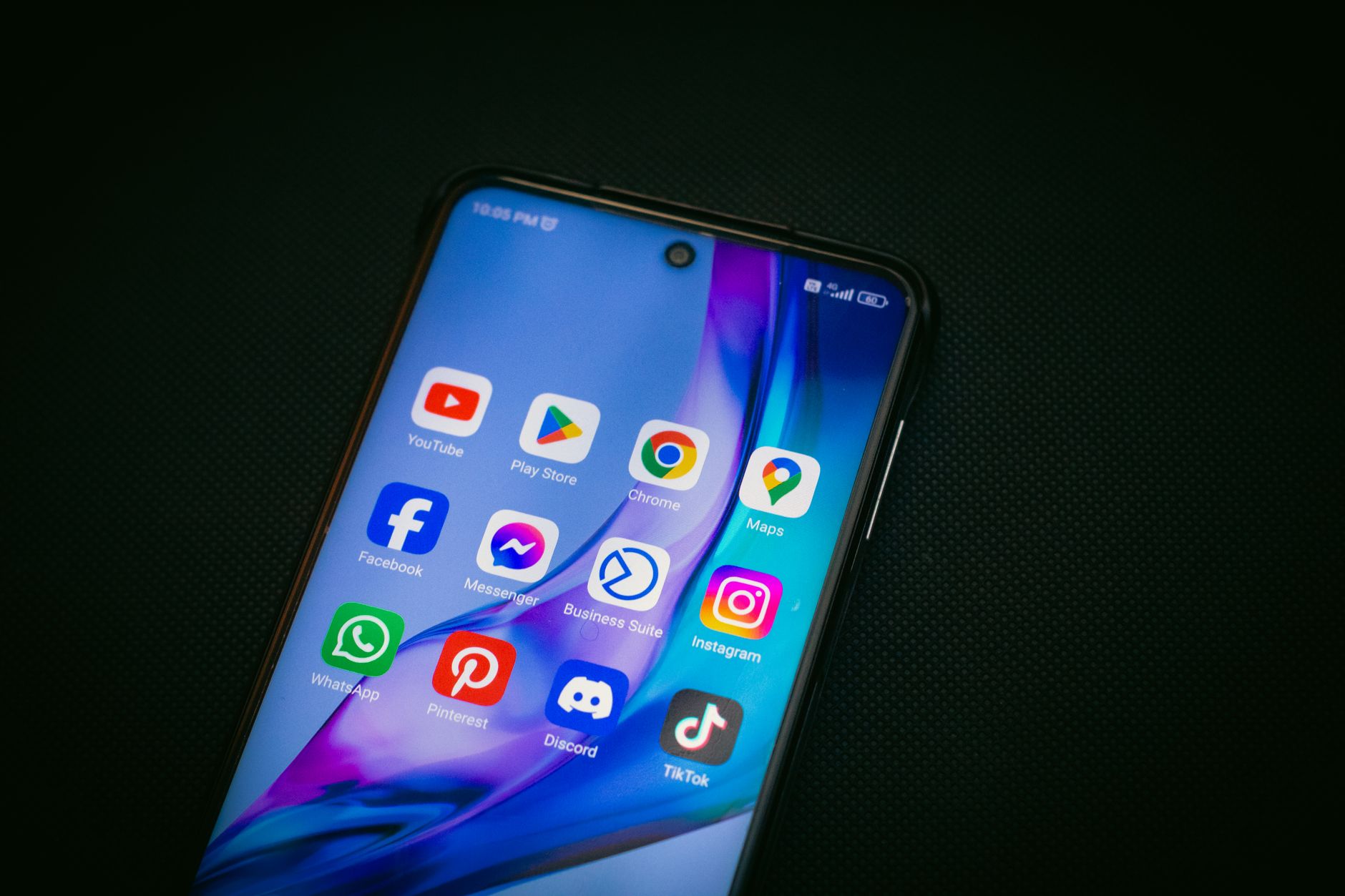 Close-up of a smartphone screen showing popular app icons like YouTube, Maps, and TikTok on a black background. — The Secret
